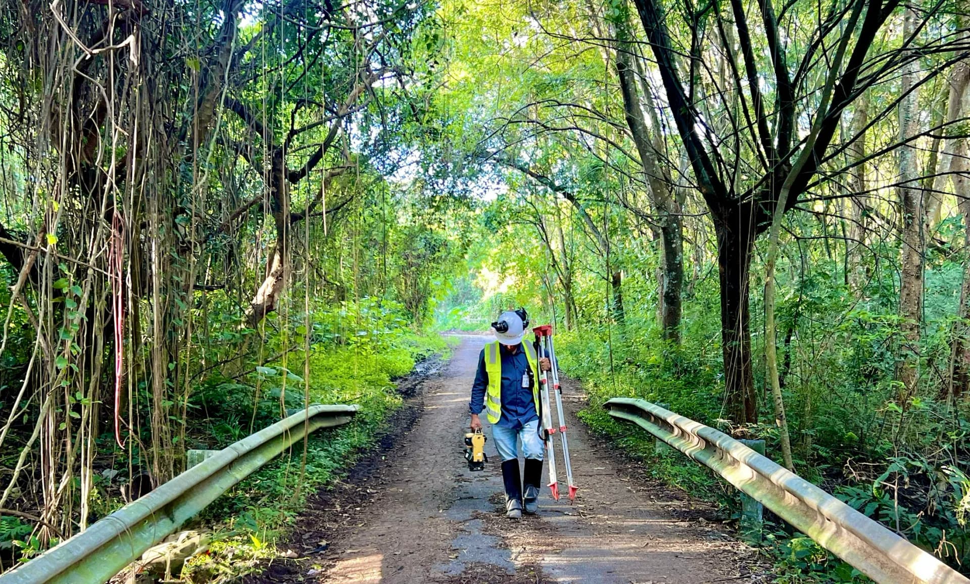 Dupla da equipe BIOMAP caminhando por estrada de mata com equipamento topográfico