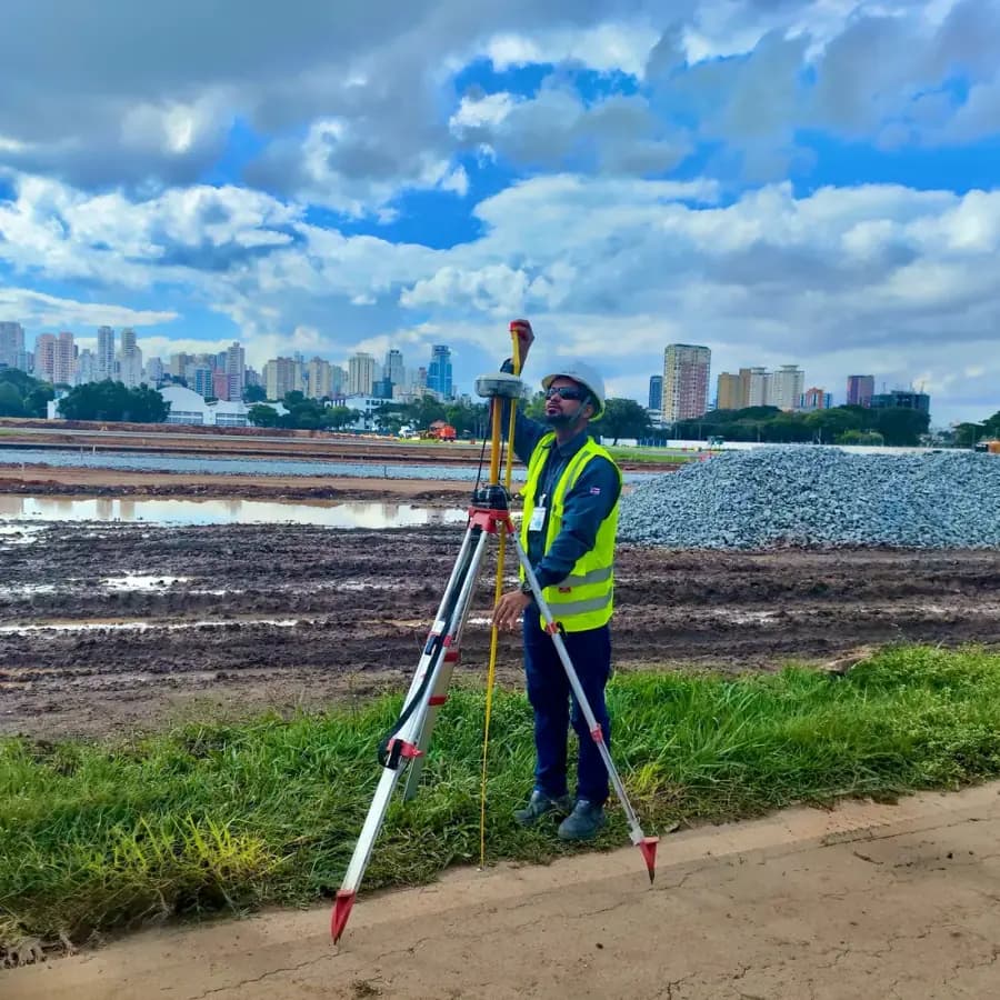 Operador BIOMAP com nível em tripé, orla e cidade ao fundo