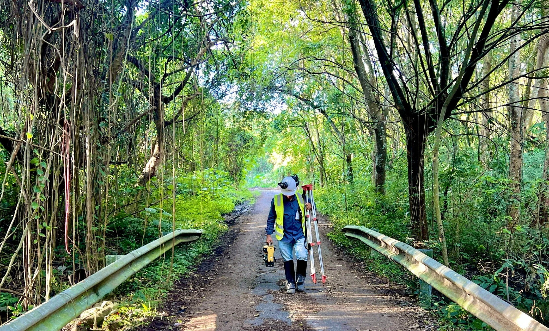 Dupla da equipe BIOMAP caminhando por estrada de mata com equipamento topográfico